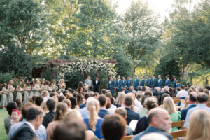 groom and best man standing at wedding lawn pergola with guests looking on